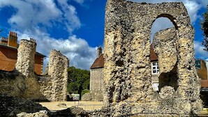 Una estructura de piedra histórica con un gran arco, rodeada de edificios modernos y un cielo despejado.