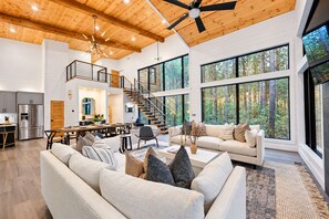 A spacious living area with a high ceiling, large windows, and a modern kitchen. - Luxury Family Cabin | Sleeps 17, Hot Tub, Games (Broken Bow)