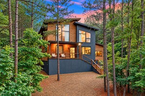 A modern two-story house with a wooden exterior, large windows, and a staircase leading to the upper level. - Family Cabin | Hot Tub, Games & Fire | Sleeps 17 (Broken Bow)