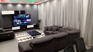 Ein modernes Wohnzimmer mit einer Eckcouch, einem Flachbildfernseher und einem gemusterten Teppich.