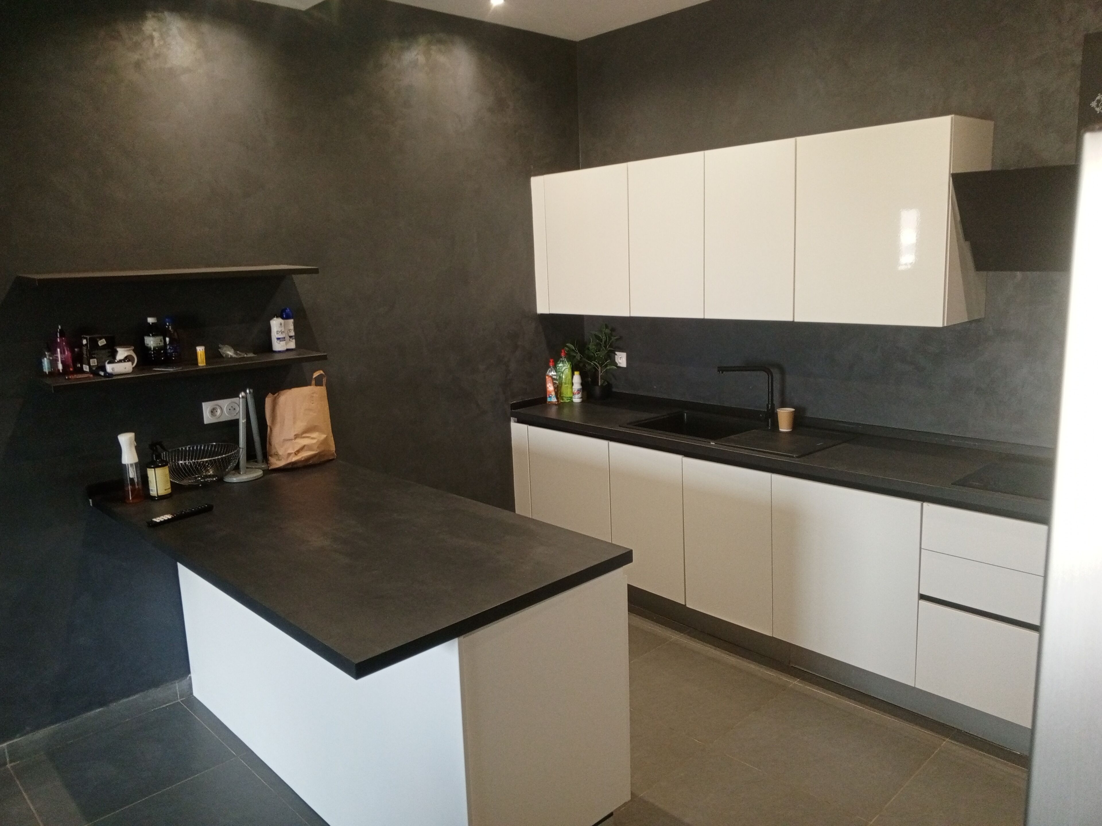 Una cocina moderna con encimeras oscuras, armarios blancos y salpicadero negro.