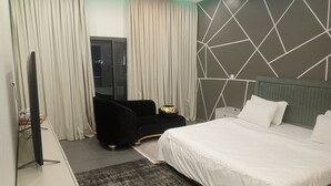 Ein modernes Hotelzimmer mit einem großen Bett, einem Flachbildfernseher, einem schwarzen Sessel und einem geometrischen Wanddesign.