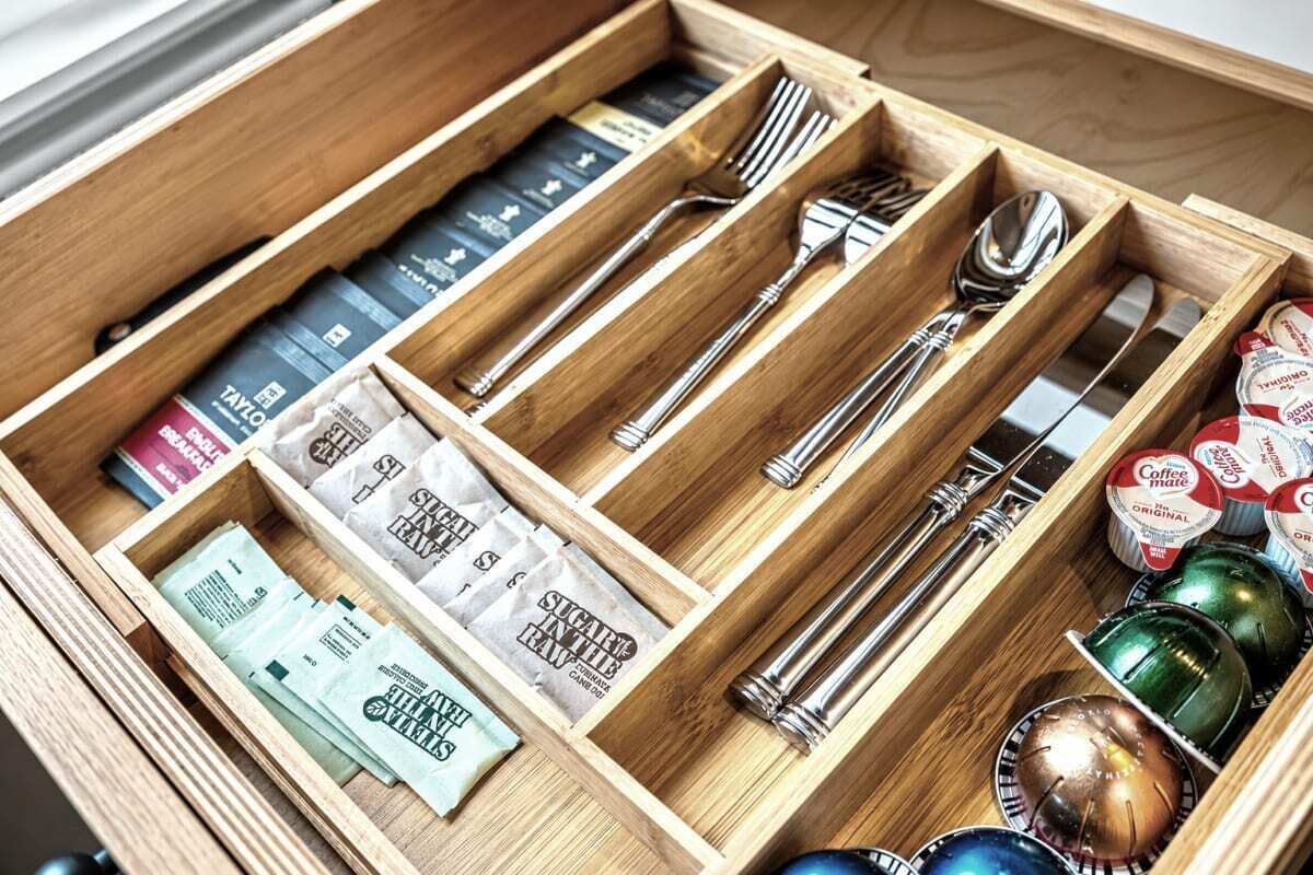 A wooden drawer with compartments containing various items including books, utensils, and coffee pods.