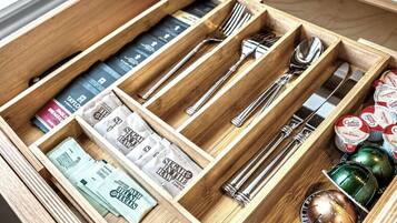A wooden drawer with compartments containing various items including books, utensils, and coffee pods.