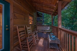 Eine Holzterrasse mit einem Korbstuhl-Tisch und -Stühlen, einer Hängeschaukel und Blick auf den umliegenden Wald.