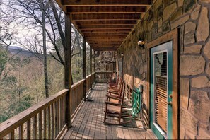 A wooden deck with a stone wall, a wooden door, and a view of the surrounding forest. - Sleeps 15, Dog Friendly Log Cabin, Hot Tub, Arcade, 4 Mi to Downtown Gatlinburg (Gatlinburg)