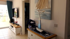 Een woonkamer met een televisie op een standaard, een schilderij van een zeilboot, een kast en een deur naar een andere kamer.