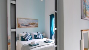 Een slaapkamer met een bed, een grote spiegel, een schilderij en een houten nachtkastje.