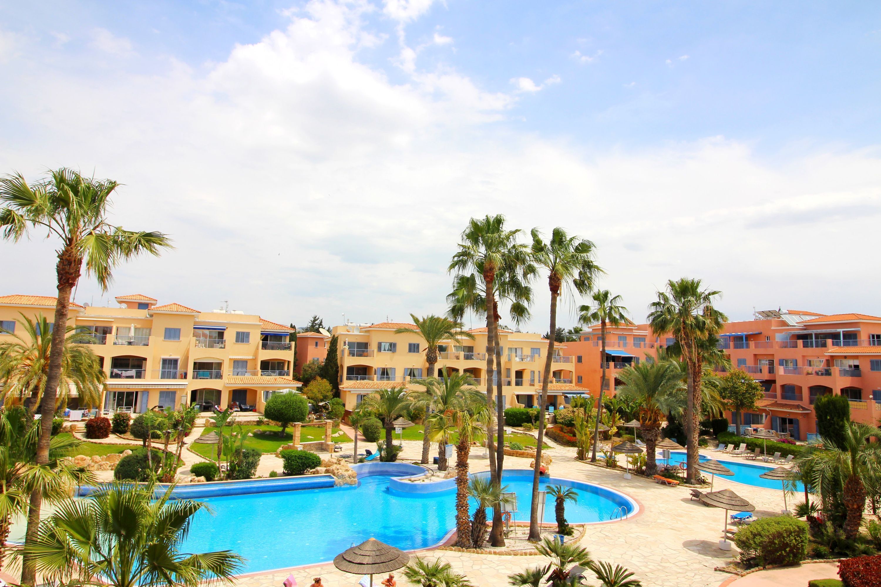 A resort with a swimming pool, palm trees, and a multi-story building with balconies.