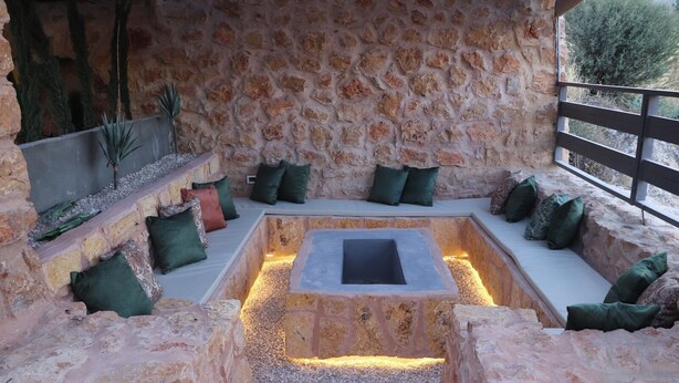 A stone-walled outdoor seating area with cushions and a central fire pit.