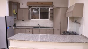 A kitchen with a granite countertop, a built-in sink, a stove, and beige cabinetry.