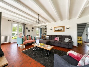 Ein großzügiges Wohnzimmer mit einer breiten Couch, einem Couchtisch und Blick ins Freie durch eine Schiebeglastür.