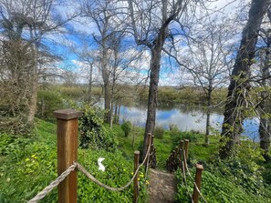 Eine Holzbrücke, die zu einem von Bäumen und Grünflächen umgebenen See führt.