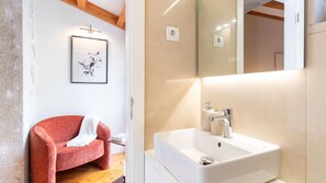 Ein modernes Badezimmer mit einem weißen Waschbecken, einem roten Stuhl und einem gerahmten Kunstwerk an der Wand.