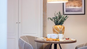 Ein Essbereich mit einem Tisch, der für das Frühstück gedeckt ist, darunter Croissants, Obst und eine Vase mit Grünpflanzen.