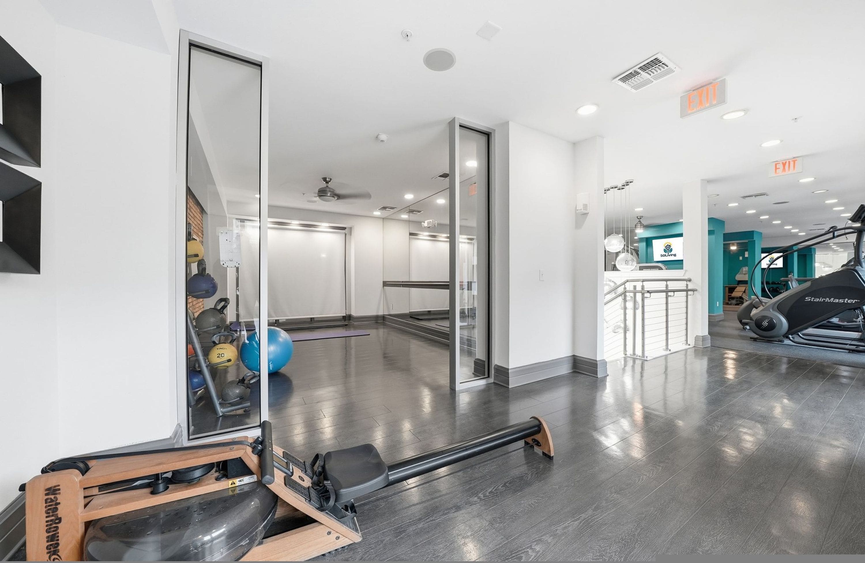 Een moderne sportschool met trainingsapparatuur, een spiegelwand en een zichtbaar vluchtroutebord.
