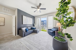 Uma sala de estar moderna com um sofá modular cinza, um espelho grande, um ventilador de teto e um vaso de planta.