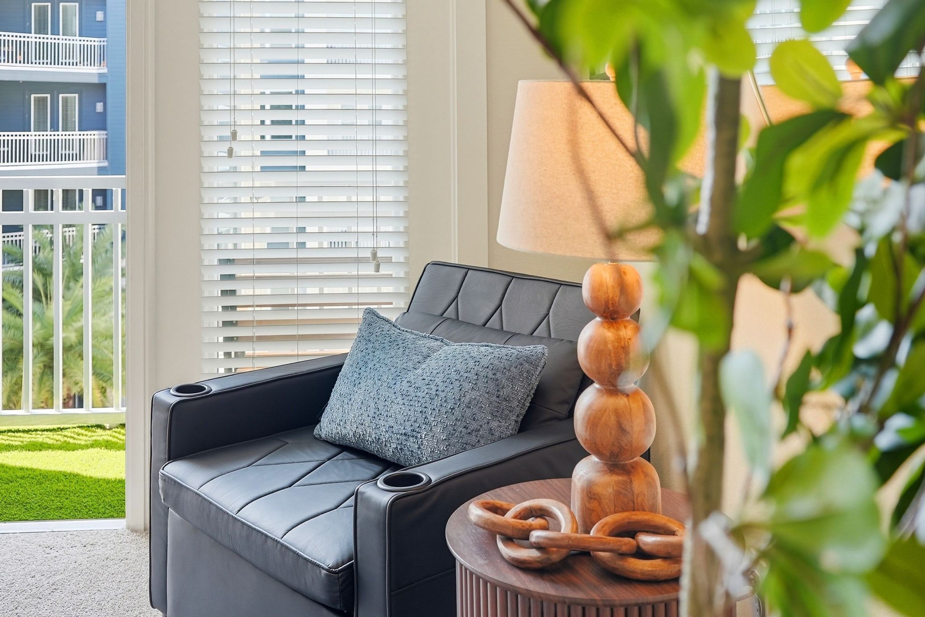 A modern lounge area with a leather sofa, a wooden side table, and a view of a building with balconies.