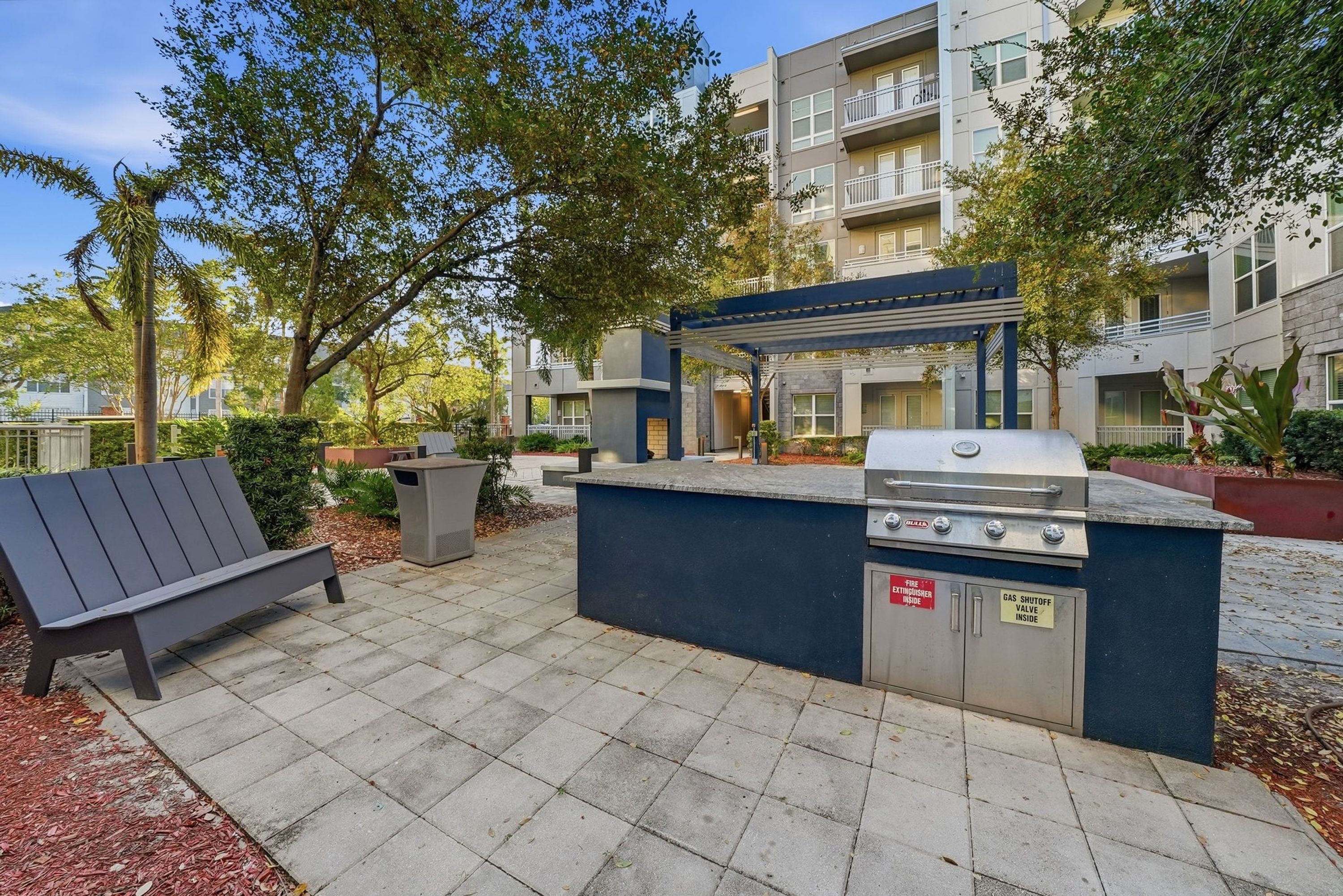 Eine Terrassenanlage im Freien mit Grill, Bank und einem mehrstöckigen Gebäude im Hintergrund.