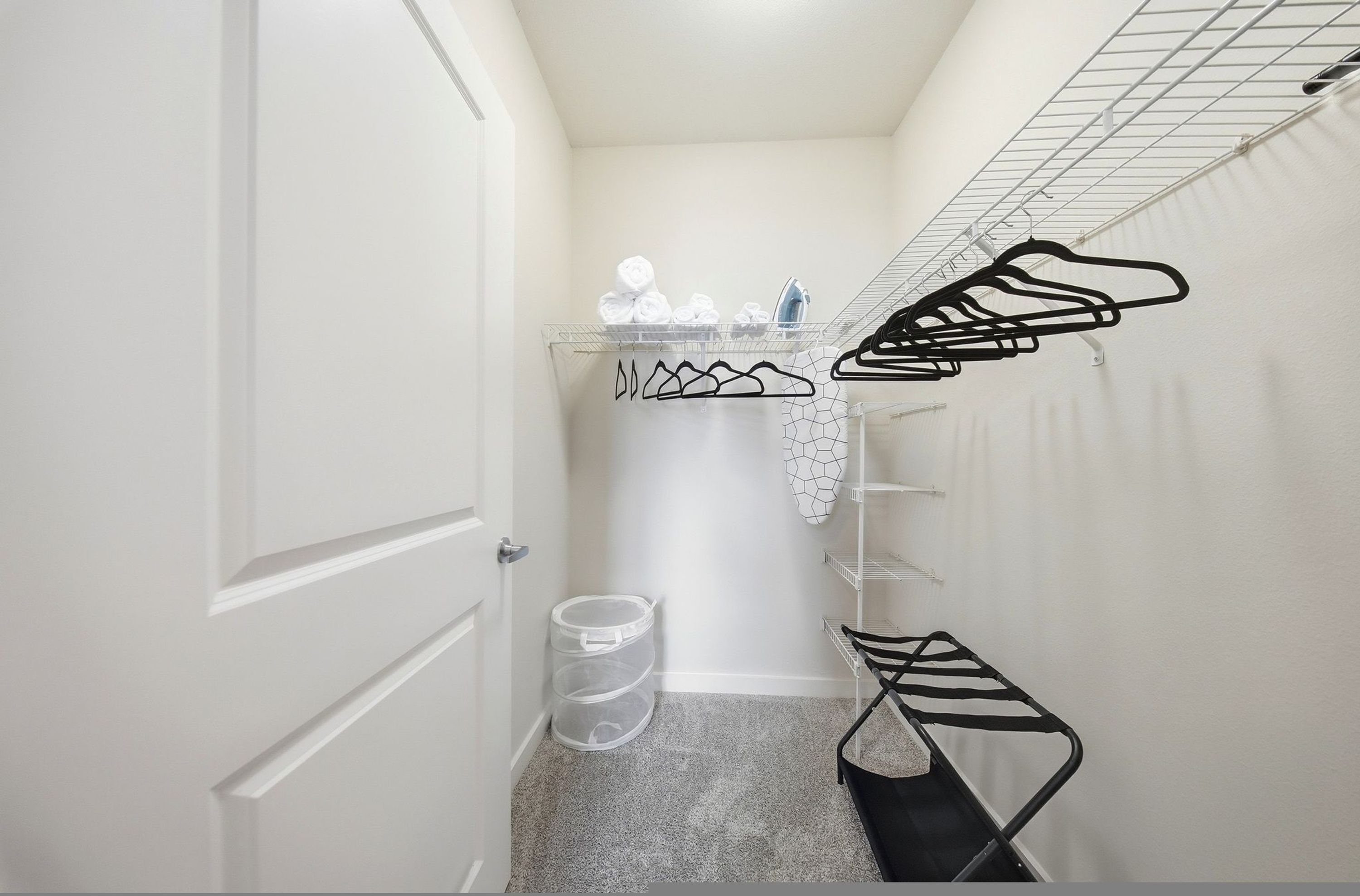 A laundry area with a drying rack, a shelf with folded towels, and a trash bin.