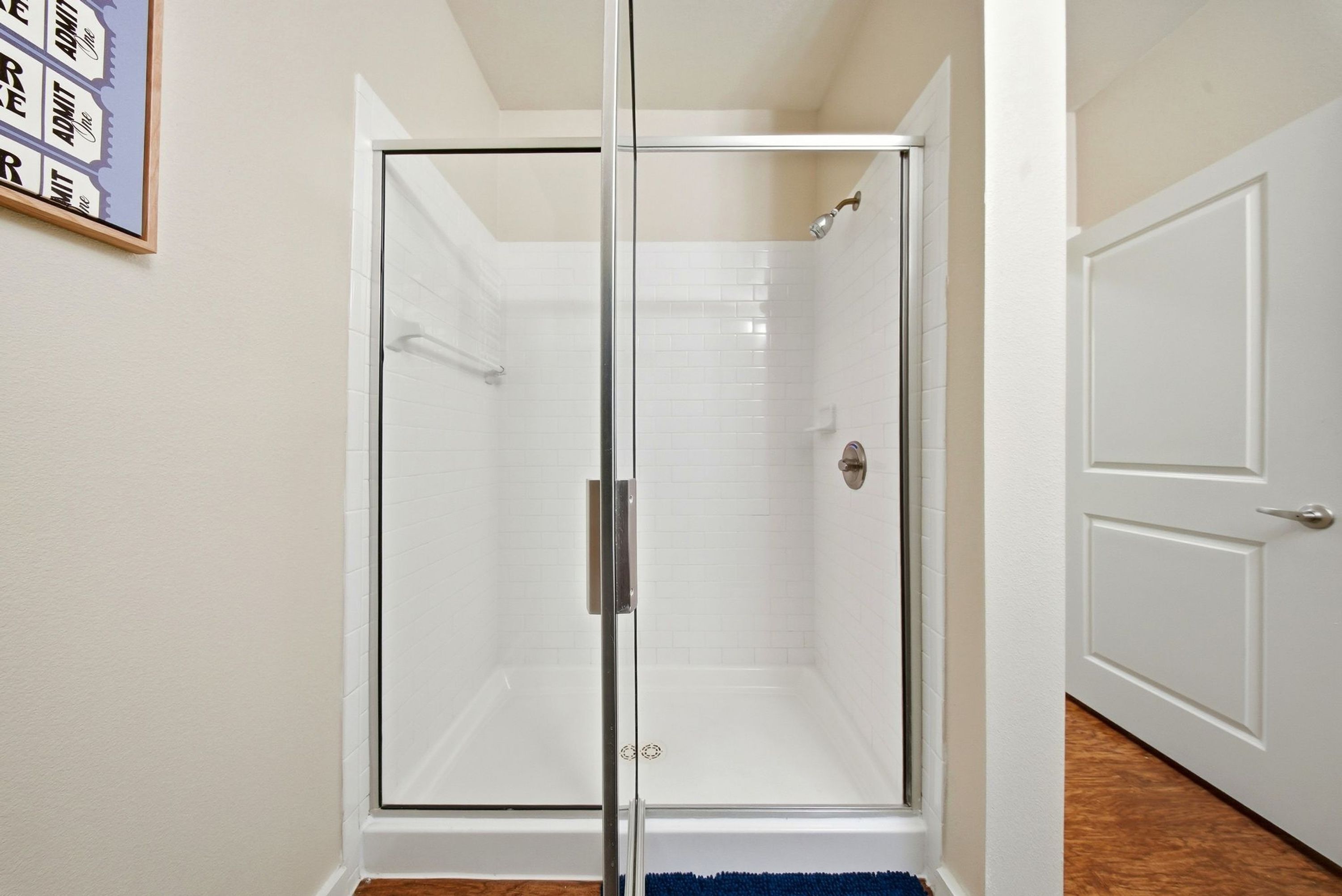 A glass-enclosed shower with a white tiled wall and a door to the right.