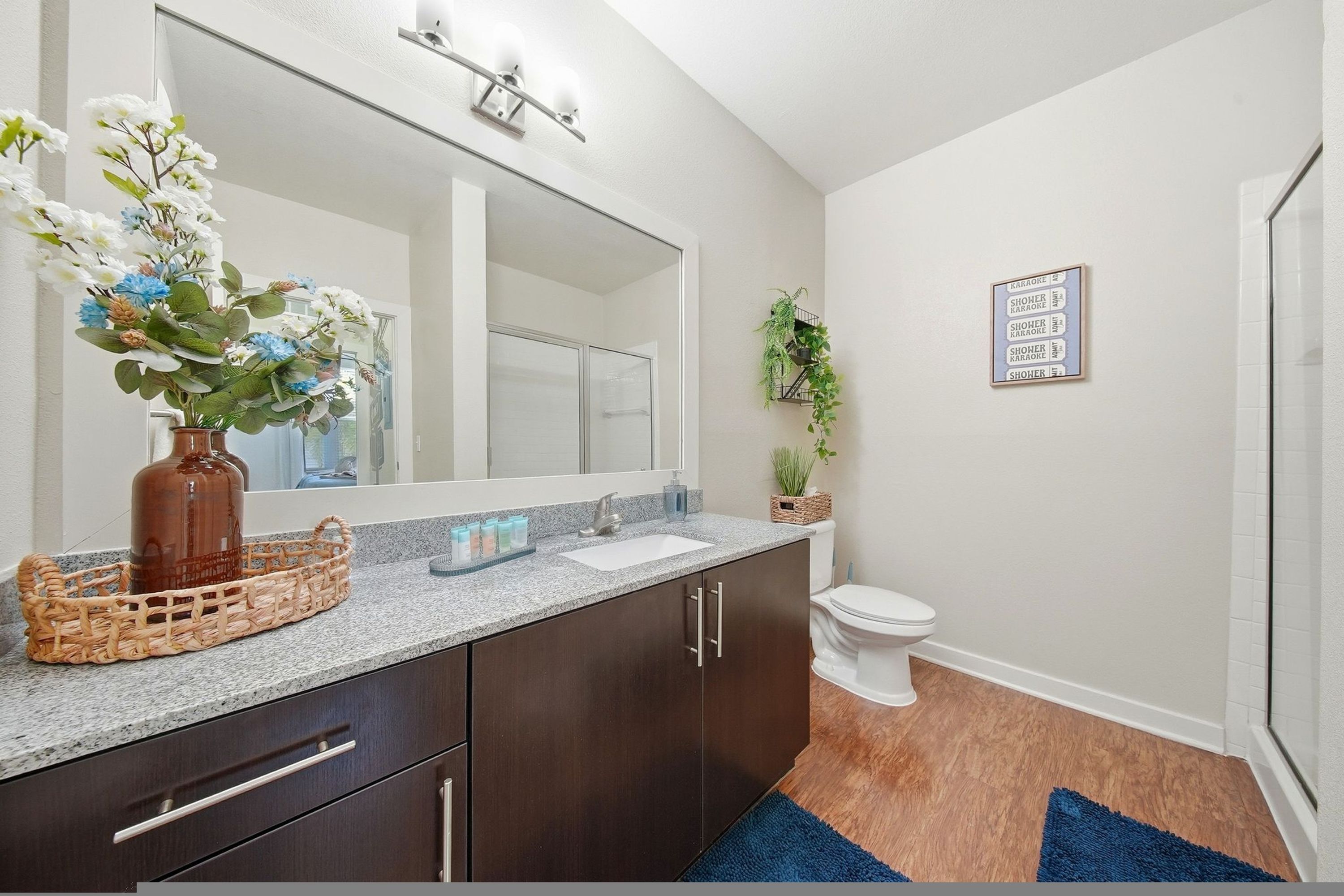 A bathroom with a large mirror, dark wooden cabinets, a white toilet, and a blue rug.