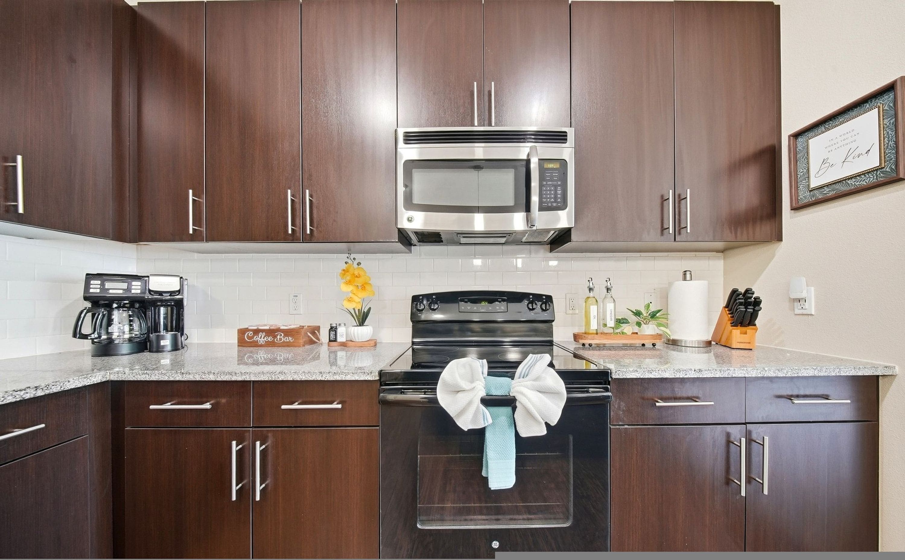 A kitchen with dark wooden cabinets, a stainless steel microwave, a black stove, and a coffee maker.