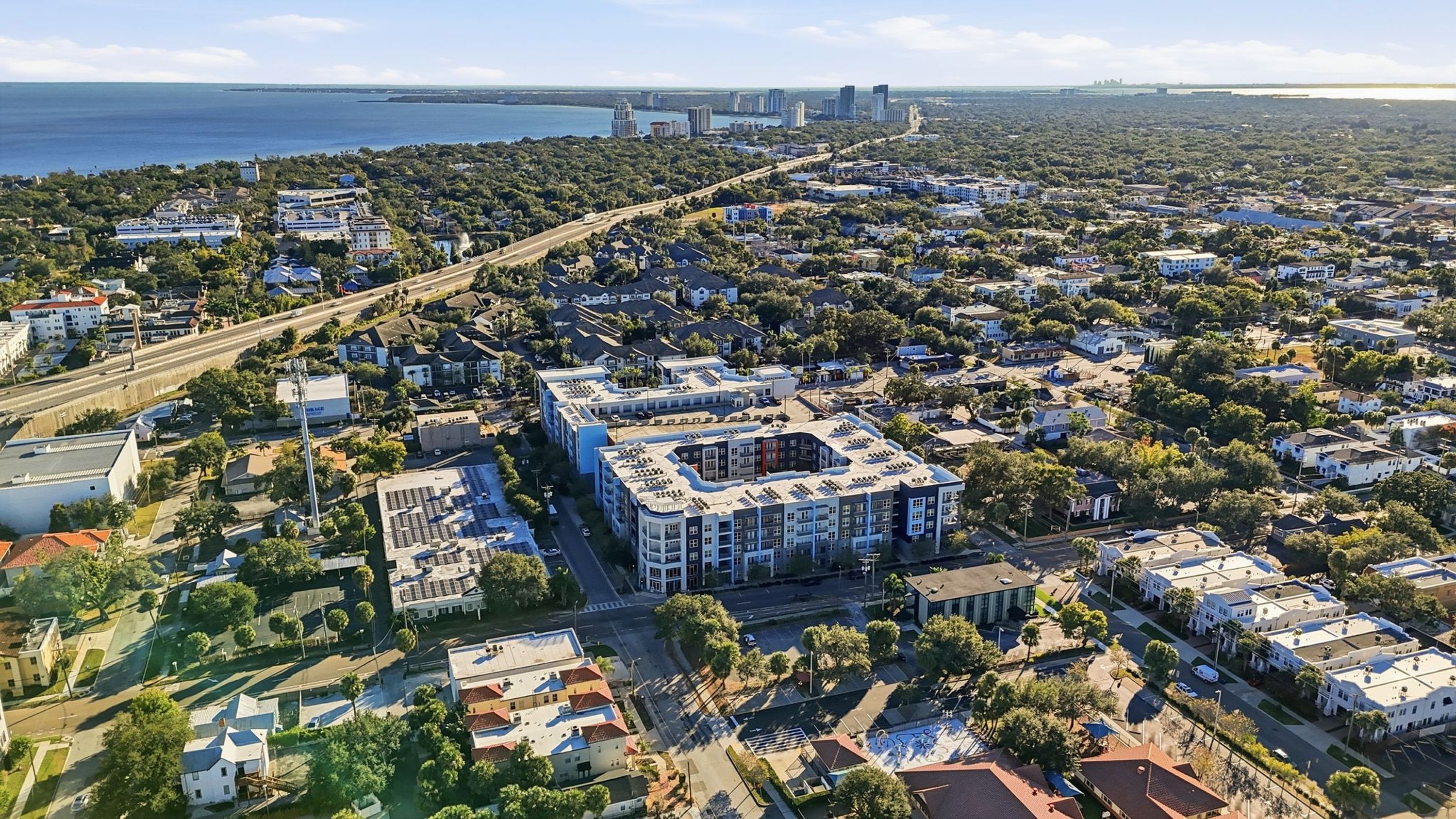 An aerial view of a residential area with a central building featuring a rooftop pool and multiple balconies.