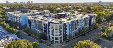 A multi-story residential building with a rooftop terrace, surrounded by greenery and a clear sky.