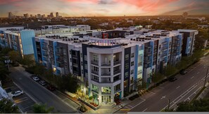 Un edificio residencial de varios pisos con terraza en el techo, estacionamiento y el horizonte de la ciudad al fondo.