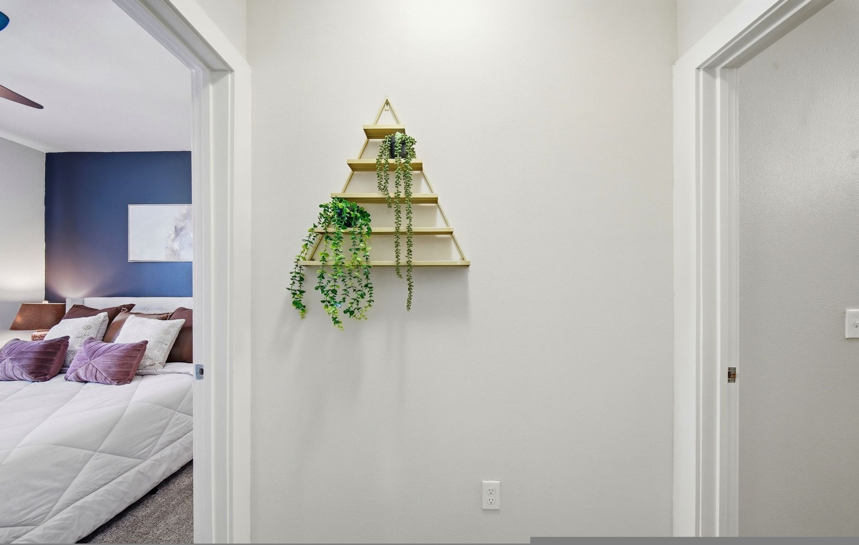 Une chambre à coucher avec un lit, des oreillers, une étagère à plantes fixée au mur et un tableau.
