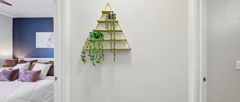 Une chambre à coucher avec un lit, des oreillers, une étagère à plantes fixée au mur et un tableau.