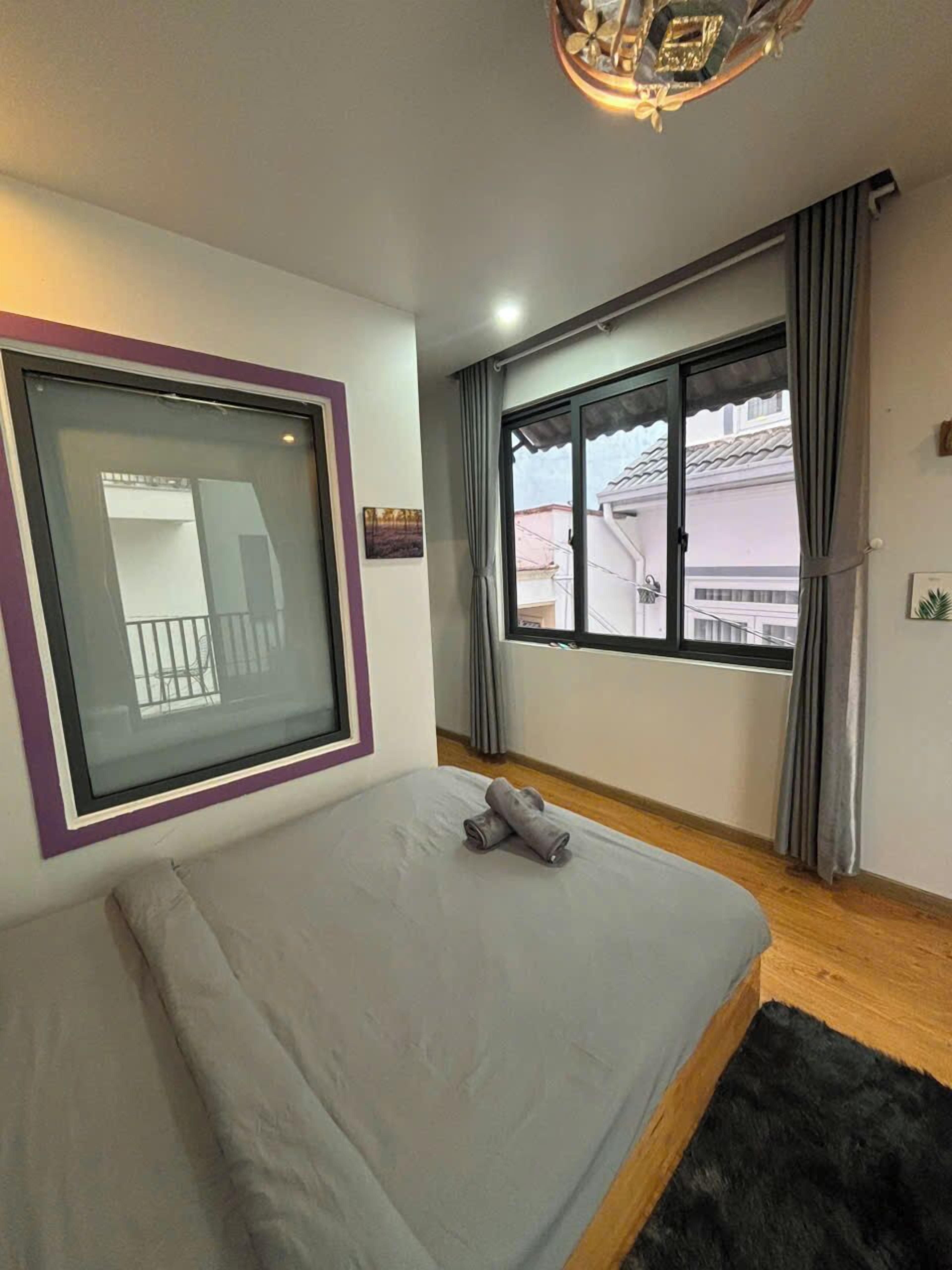 A bedroom with a bed, a window with curtains, a ceiling light fixture, and a view of the outside.