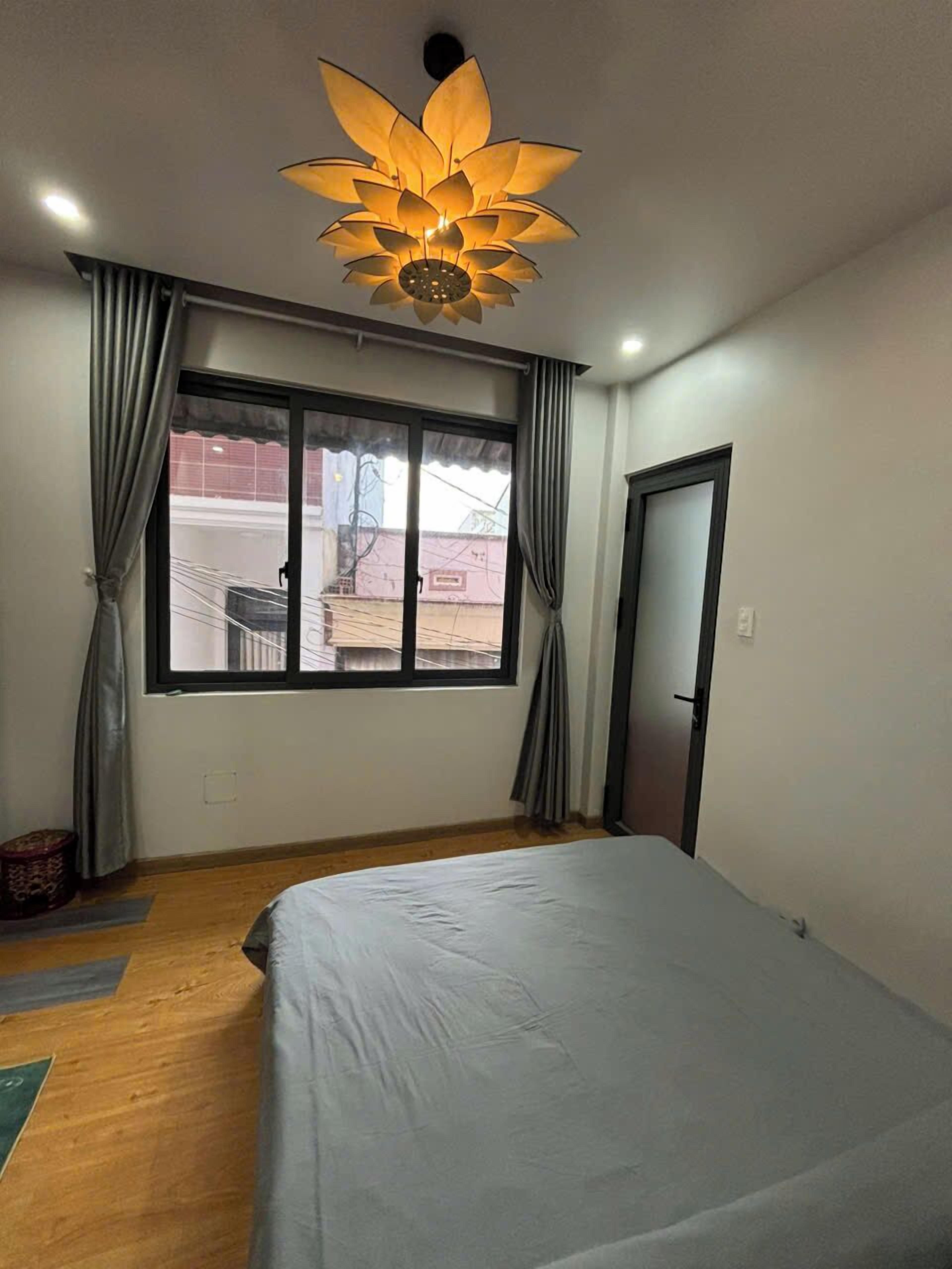 Un dormitorio con cama, ventana con cortinas, lámpara de techo y puerta.