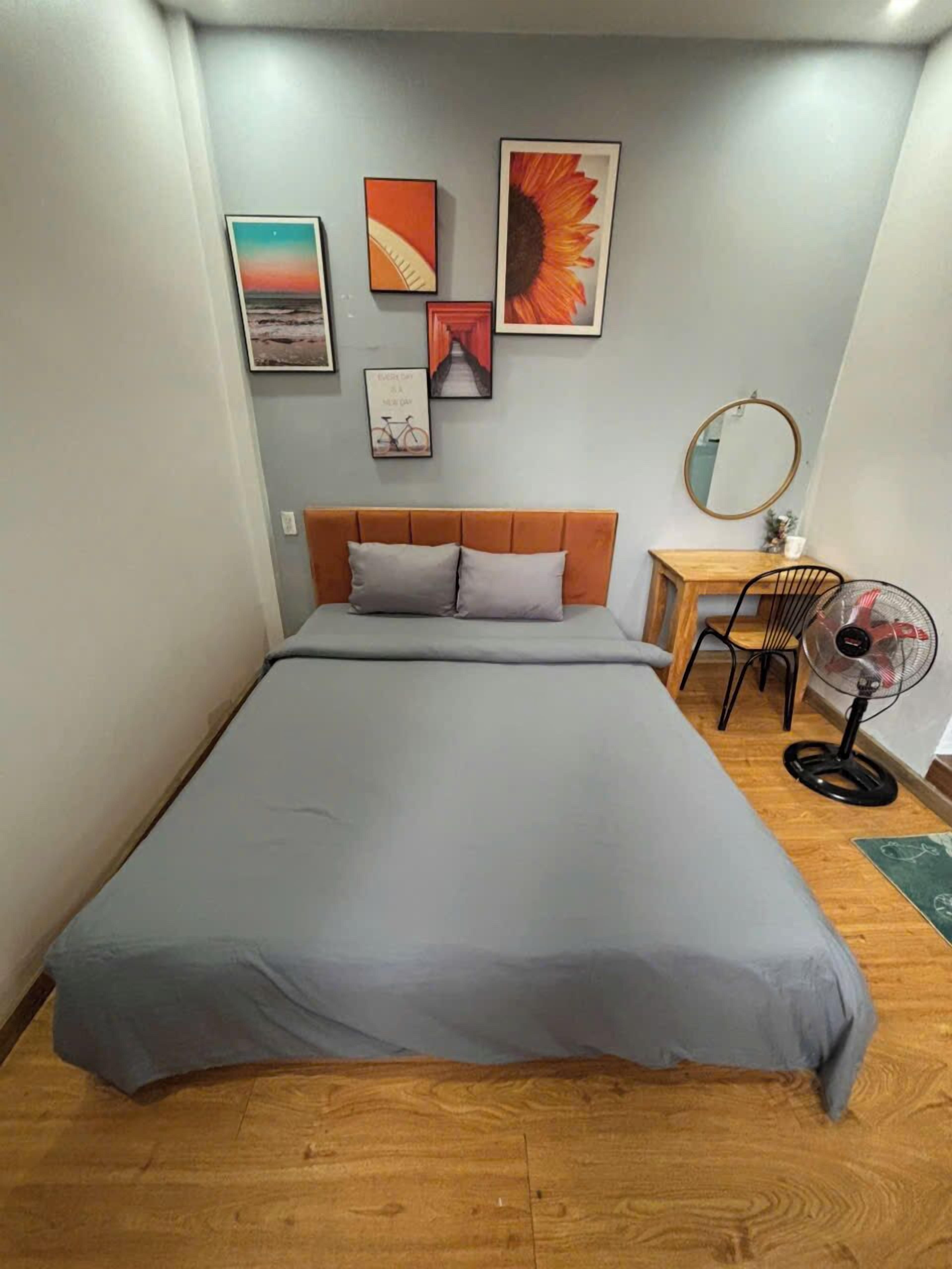 A bedroom with a bed, a chair, a desk, a mirror, and wall art.