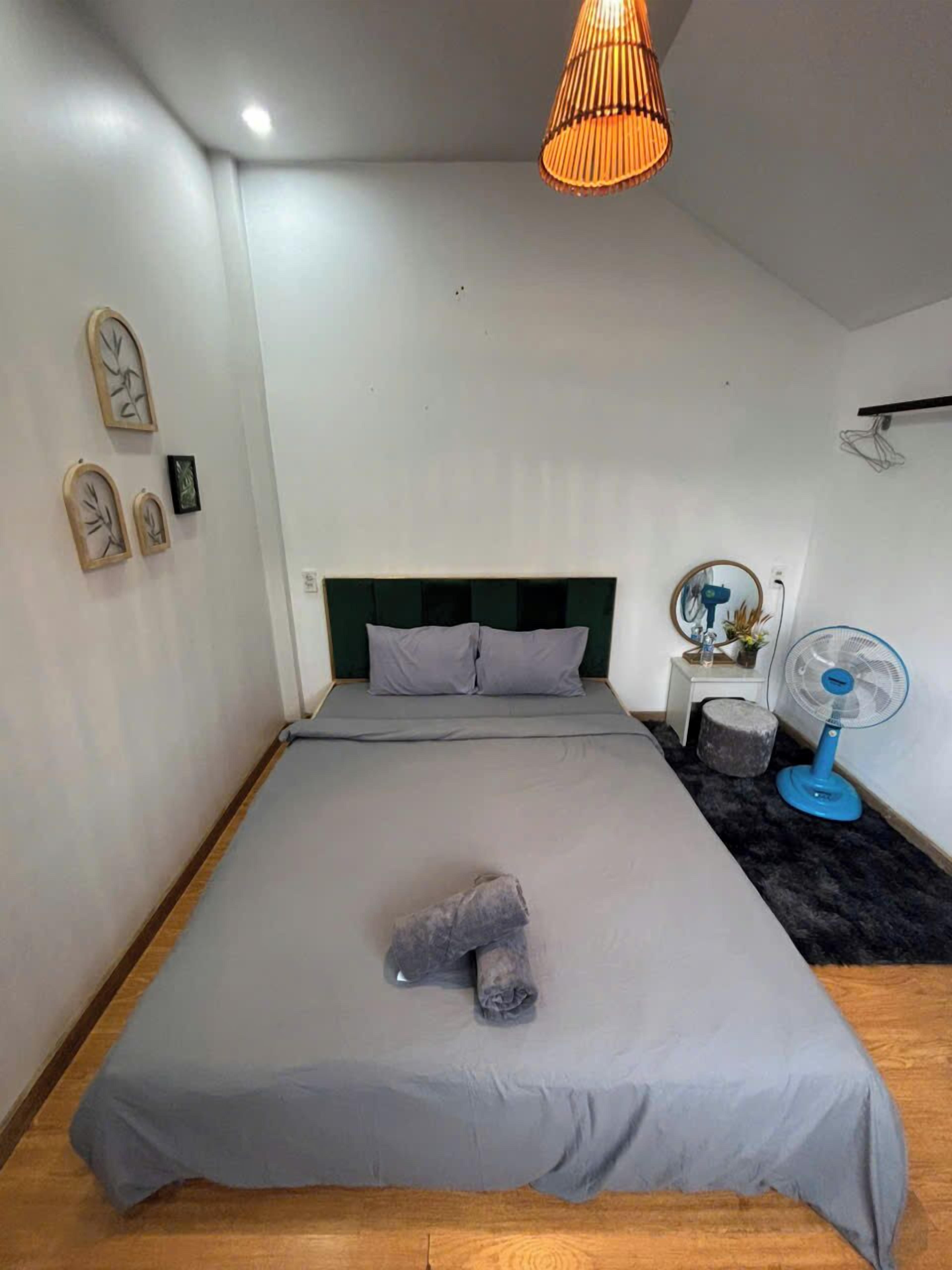 A bedroom with a bed, a bedside table, a mirror, a wall-mounted fan, and a hanging light fixture.