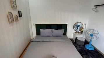 A bedroom with a bed, a bedside table, a mirror, a wall-mounted fan, and a hanging light fixture.