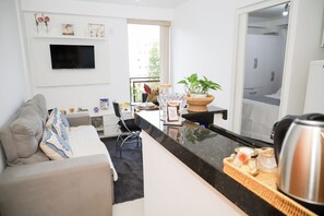 A modern living room with a sofa, a coffee table, a TV mounted on the wall, and a kitchen area with a counter and a kettle. - Cozy apartment 702/703 North, 3 min from Mané Garrincha Stadium, 5 min from Ulysses Guimarães Stadium. (Brasília)
