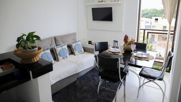 Een moderne woonkamer met een bank, een eettafel, stoelen, een aan de muur bevestigde televisie en een balkon met uitzicht.