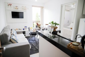A modern kitchen with a flat-screen TV, a dining area with a sofa, and a view of the outdoors. - Cozy apartment 702/703 North, 3 min from Mané Garrincha Stadium, 5 min from Ulysses Guimarães Stadium. (Brasília)