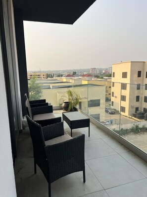 Ein Balkon mit Korbmöbeln, einem Blumentopf und Blick auf umliegende Gebäude.