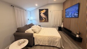 A modern room with a bed, sofa, and a small table. There is a painting on the wall, a TV, and a lamp.