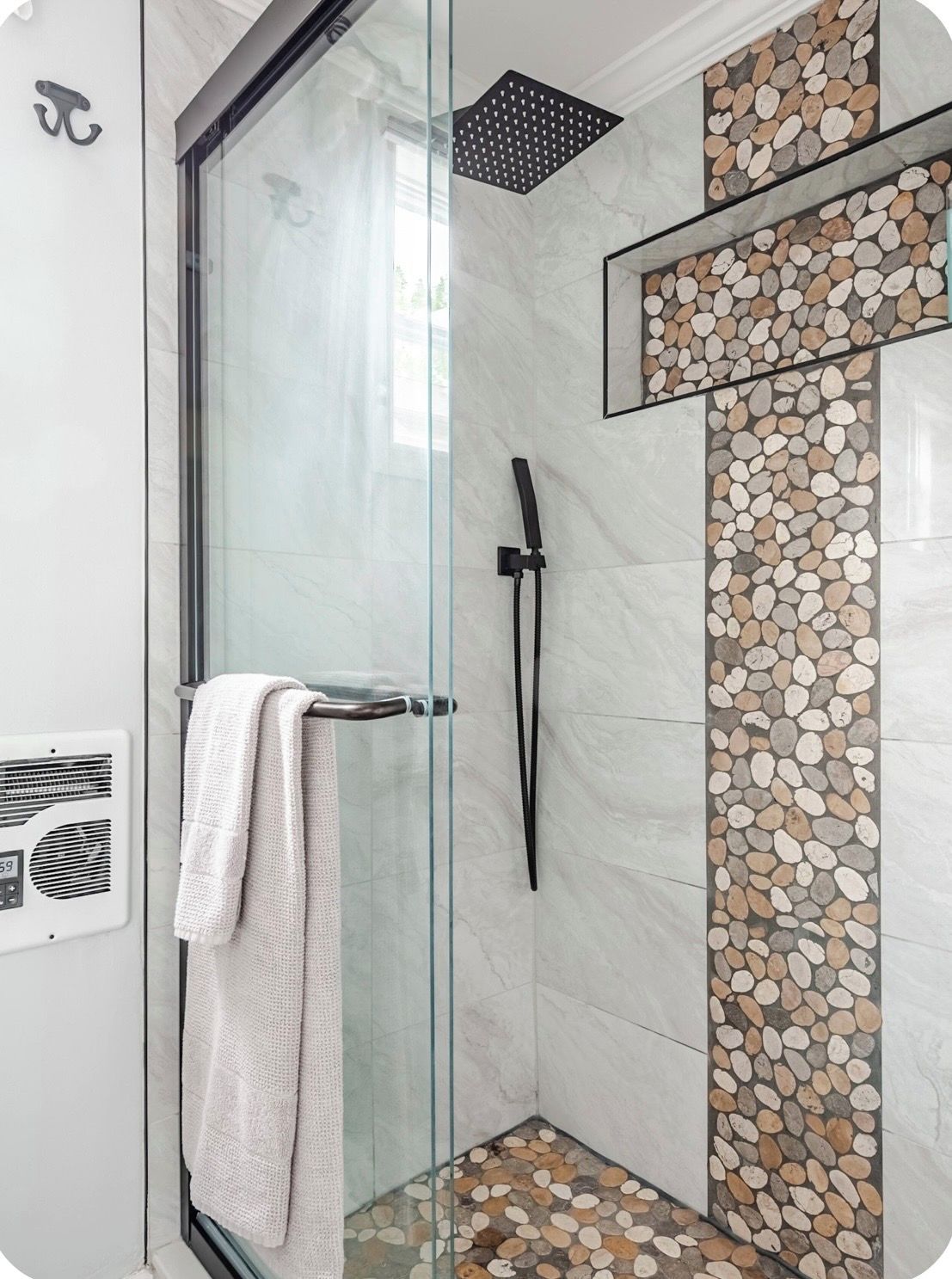 Une douche fermée par des parois en verre, dotée d’un pommeau de douche à main et d’un porte-serviettes.