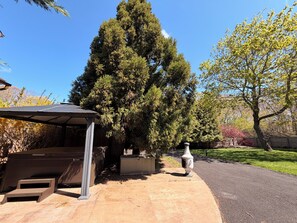 A covered outdoor area with a stone structure, a tall tree, and a paved path.