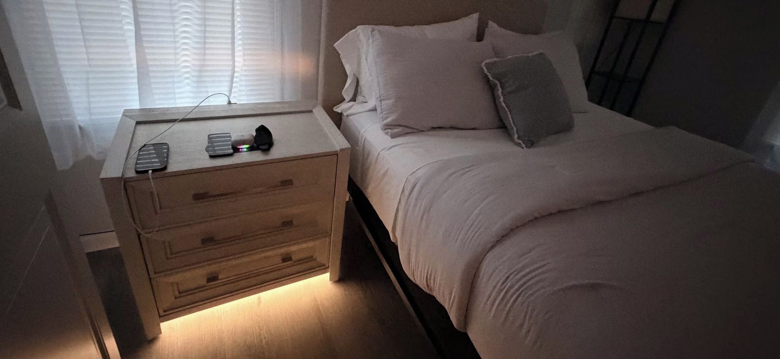 A bedroom with a bed, a bedside table with a lamp, and a window with blinds.