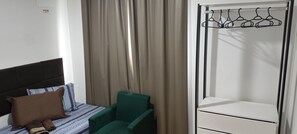 A hotel room with a bed, a green chair, a wardrobe, and a curtain. - Cabo Branco Beach. Two-Bedroom Apartment. Up to 7 people. (João Pessoa)