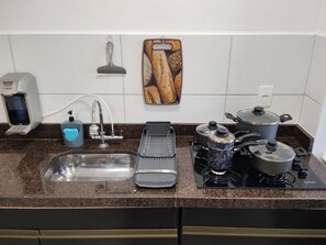 Una cocina con un lavabo, un escurreplatos, una cafetera y una estufa.