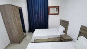 A bedroom with two beds, a wardrobe, a window with curtains, and an air conditioning unit.
