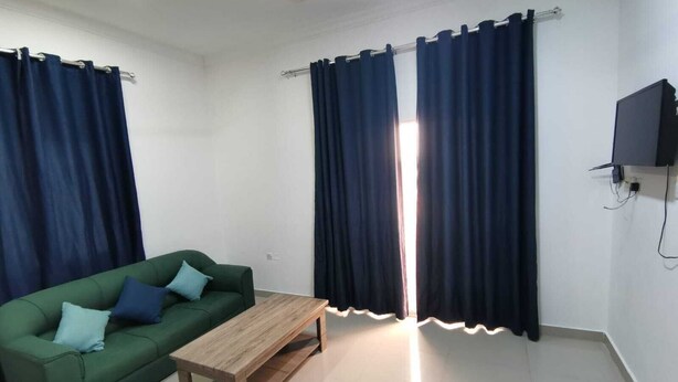 A room with a green sofa, a wooden coffee table, and dark curtains.