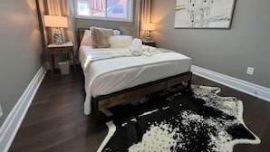 A bedroom with a bed, two bedside tables, a window, a painting, and a black and white rug. - Dreamy Escape | Cozy & Stylish Stay for Two (London)